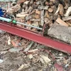 Máy bổ củi thủy lực nằm ngang cạnh bãi củi, với khúc gỗ lớn trên thân máy